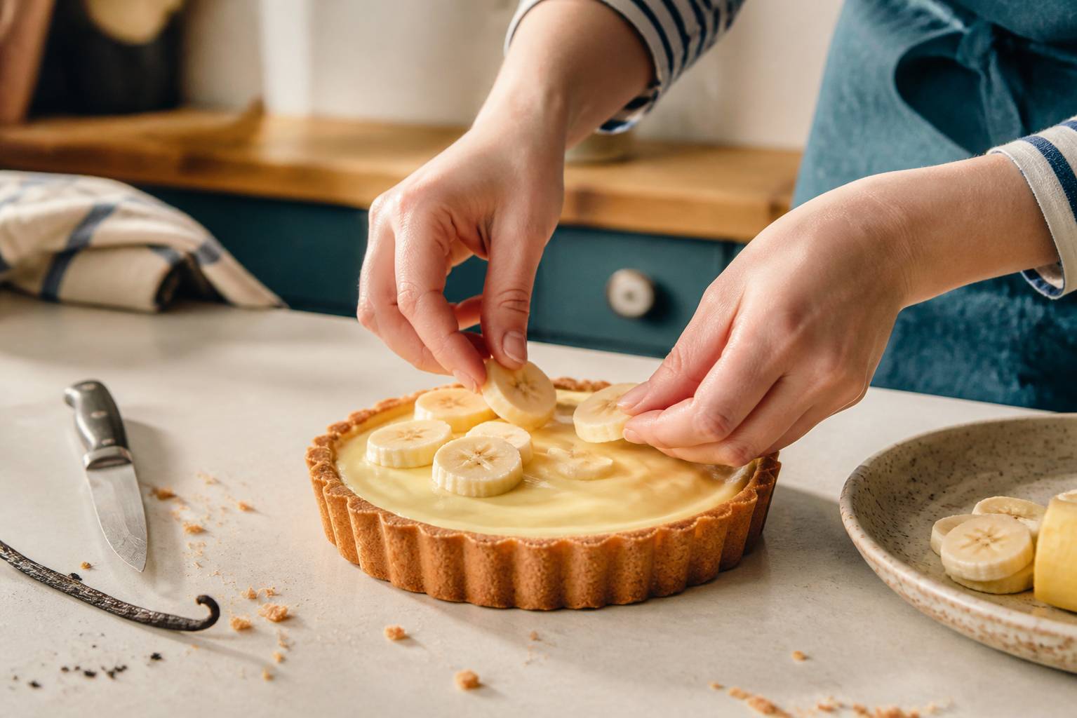 Mains déposant des tranches de banane sur une tartelette garnie de crème